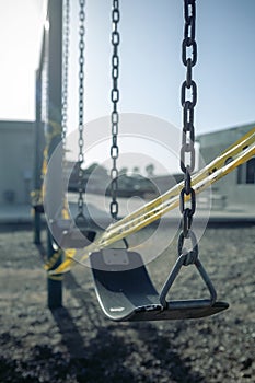 Empty plastic swings on playground with caution tape, selective focus