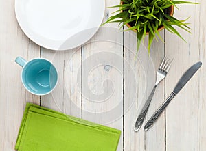 Empty plate, cup and silverware over white wooden table background