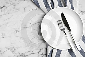 Empty plate with cutlery and fabric on marble table, flat lay. Space for text