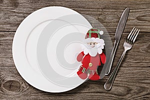 Empty plate and cutlery on a wooden table with copy space. Soft Christmas toy Santa Claus. Food background