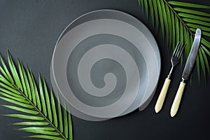 Empty plate on a dark background. Empty gray ceramic plate with a knife and fork for food and dinner on a dark beautiful