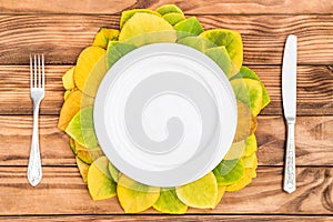 Empty plate with fork, knife and autumn leaves on wooden table. Top view