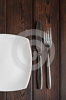 Empty plate, fork and knife on dark wood background