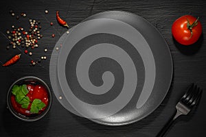 Empty plate, fork, tomato, ketchup and spices on black background top view