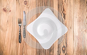 Empty plate with knife and fork on wooden table