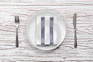 Empty plate napkin fork knife silverware white wooden table background