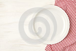 Empty plate with red napkin over white wooden table background.