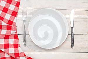 Empty plate, silverware and towel over wooden table background