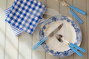 Empty plate, silverware and towel over wooden table background. View from above, blue colors