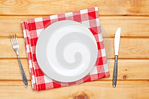 Empty plate, silverware and towel over wooden table background