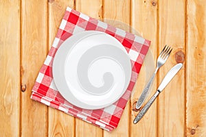 Empty plate, silverware and towel over wooden table background