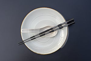 Empty plate, spoon and chopsticks on black table in asian restaurant, close up