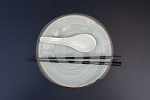 Empty plate, spoon and chopsticks on black table in asian restaurant, close up