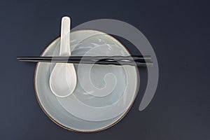 Empty plate, spoon and chopsticks on black table in asian restaurant, close up