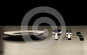 Empty plate with spoon, knife and fork on a black background