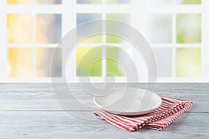 Empty plate with striped tablecloth on wooden table over beautiful window background