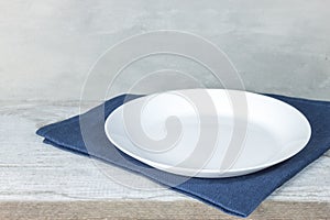 Empty plate on tablecloth on wooden table over grunge blue background