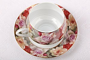 Empty porcelain tea cup with saucer and floral pattern on a table with white tablecloth