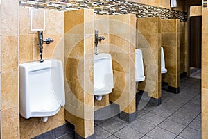 Empty public men`s restroom interior with porcelain urinals with