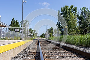 Empty railroad tracks with yellow safety line - surrounded by greenery - clear blue sky