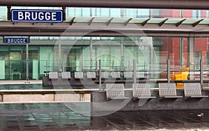 Empty railway station building and platform with glass walls and sign Brugge and waiting bench with seats.