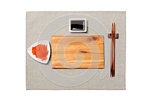 Empty rectangular brown wooden plate with chopsticks for sushi, ginger and soy sauce on grey napkin background. Top view with copy