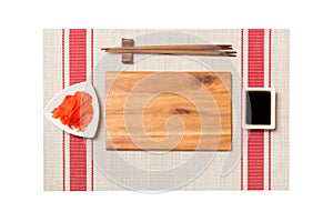 Empty rectangular brown wooden plate with chopsticks for sushi, ginger and soy sauce on sushi mat background. Top view with copy