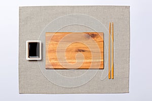 Empty rectangular brown wooden plate with chopsticks for sushi and soy sauce on grey napkin background. Top view with copy space