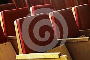 Empty red chairs in theatre. Old tired cinema seats covered with worn red velvet. Red theater seats.