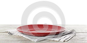 Empty red plate and napkin on table against white background