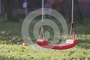 Empty red swing on children playground in the park in autumn season. Missing child.