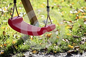 Empty red swing on children playground in the park in autumn season. Missing child