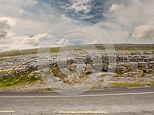 Empty road in Burren National park, Ireland, Rough stone terrain, Traditional stone fence. Cloudy sky in the background