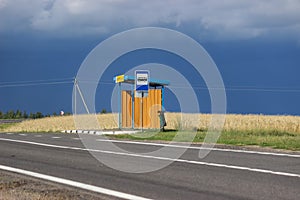 Empty road and a bus stop in the middle of a ripe field before a thunderstorm