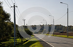 Empty road with lampposts along a field with a Tractor in the distance