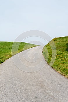 Empty road leading into the blue sky along green grassy shoulders or embankments