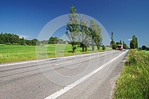 Empty road lined with poplar alley in the countryside, in the distance passing red truck