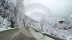 Empty road in the mountains during winter with snow covered trees on the side.