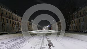 An empty roadway in a winter city at night. Traffic light blinks orange. Urban lighting. Weather conditions. Old three