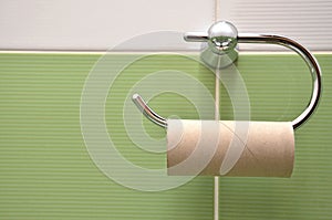 Empty roll on toilet paper holder with white and green tiles in background