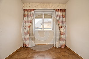 Empty room with aluminum and glass windows, dark stoneware floors and curtains with sheers