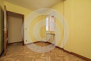 Empty room with an aluminum window, radiator in a niche, varnished oak parquet flooring and wooden doors