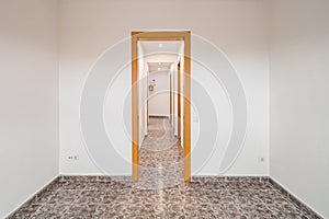 Empty room in apartment with long corridor, tiled floor and white walls