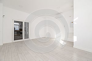 An empty room in an apartment with white walls, light wooden floors, air conditioning high on the wall and double white aluminum