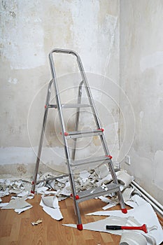 Empty room with bare walls ladder and old wallpaper scraps on floor during redecoration photo