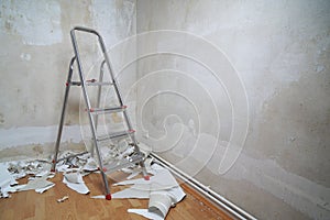 Empty room with bare walls ladder and old wallpaper scraps on floor during redecoration wth copy space photo