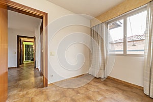 Empty room with brown stoneware floors, window with curtains and access door to other rooms