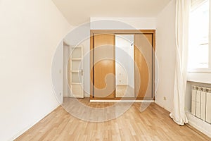 Empty room with a built-in wardrobe with sliding mirror doors combined with wood and a white wooden door and laminated flooring