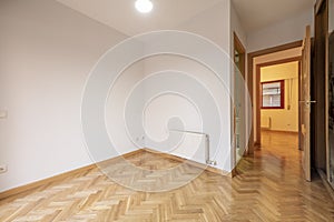 Empty room with built-in wardrobe with sliding mirror doors, white aluminum radiator, en-suite bathroom and herringbone-laid oak