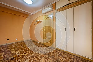 An empty room with a built-in wardrobe with white doors and a mezzanine with a trunk, oak parquet floors laid in a checkerboard